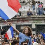Young girl with curly hair raises a large French flag amid a crowded protest at a monument. - برفيلكس - brieflex