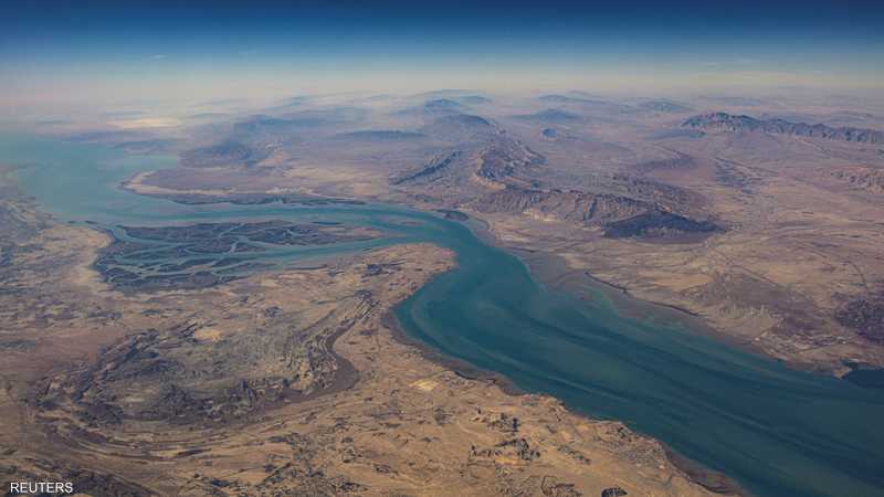 Aerial view of a blue-green river winding through a dry, desert landscape with canyons and distant mountains. - برفيلكس - brieflex