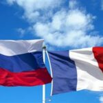 Two national flags waving in the wind: Russia on the left (white-blue-red horizontal stripes) and France on the right (blue-white-red vertical stripes) against a blue sky. - برفيلكس - brieflex