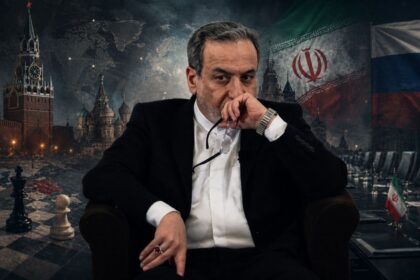 Man in a black suit sits in a chair, holding glasses to his mouth, with a backdrop showing a world map, Moscow landmarks, and flags.