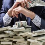 Person in a suit counts and fans a stack of US dollar bills on a table. - برفيلكس - brieflex