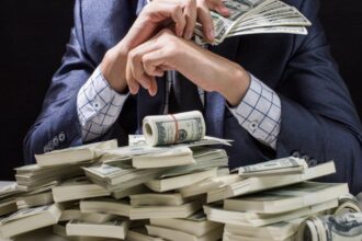 Person in a suit counts and fans a stack of US dollar bills on a table.