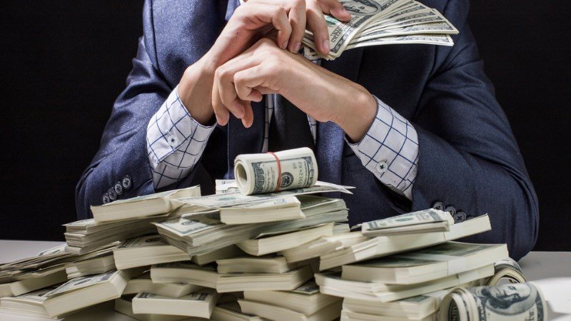 Person in a suit counts and fans a stack of US dollar bills on a table. - برفيلكس - brieflex