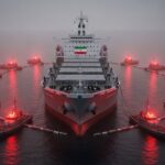Large cargo ship anchored in calm sea, Iran flag on stern, surrounded by red-lit tugboats. - برفيلكس - brieflex
