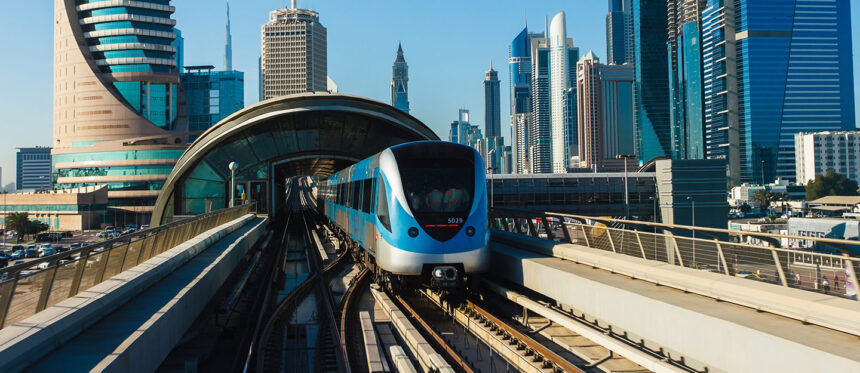 Blue and white metro train on an elevated track approaching a curved glass station, with a skyline of tall glass towers behind. - برفيلكس - brieflex