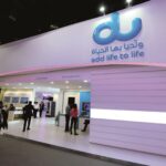 Trade show booth featuring a large blue 'du' logo and the slogan 'add life to life' on a curved purple wall, with attendees walking nearby. - برفيلكس - brieflex